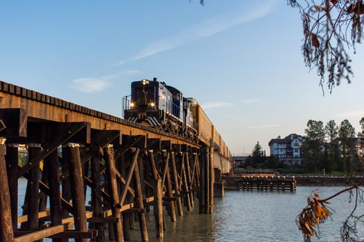"New Westminster, British Columbia/Canada - 8/3/2019: New Westminster Quay old wooden train bridge with Canadian Trail link driving across in evening sunshine and blue summer sky."