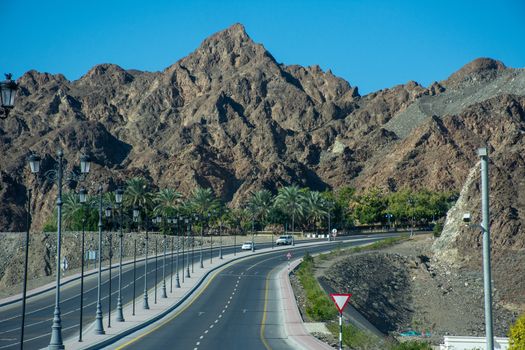 "Muscat, Muscat/Oman - 12/17/2019: Mountain highway road with rocky mountains and blue sky in Muscat, Oman near Muttrah Souq and Old Town. "