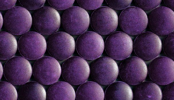a seamless hexagonal pattern of many purple organic spirulina tablets laid tight in one layer on flat surface.