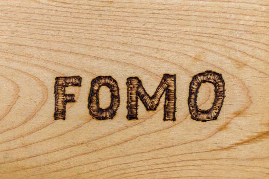 abbreviation FOMO - fear of missing out - burnt by hand on flat wooden surface.
