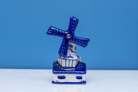 Delft Blue Figurine of blue windmill on a white shelf with a blue background. A souvenir from Holland/Netherlands.