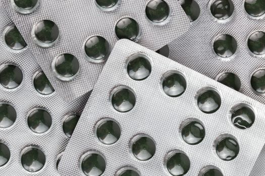 unopened green spirulina pills in medical blister packs close-up with directly above flat lay perspective and full frame composition