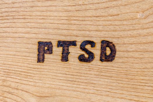 an abbreviation PTSD - post traumatic stress disorder - burned by hand on flat wooden board.