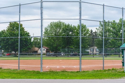 "Brighton, Ontario/Canada - 07/22/2019: Baseball or softball diamond through a fence in  park in a small town Canadian city of Brighton near Pesquile Lake Provincial Park ."
