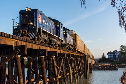 "New Westminster, British Columbia/Canada - 8/3/2019: New Westminster Quay old wooden train bridge with Canadian Trail link driving across in evening sunshine and blue summer sky."