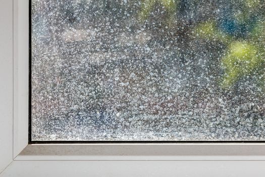 dirty window glass and part of white plastic frame at sunny summer or spring weather close-up with selective focus and blur.