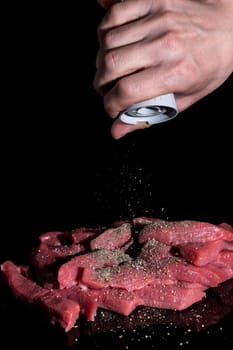 Pepper the cut pieces of meat. Cooking at home, in the restaurant. Recipe, menu, chef. Ingredients for cooking