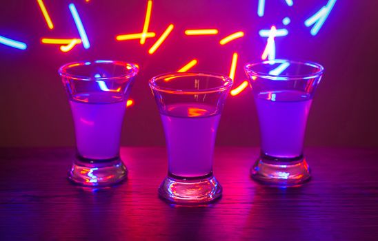 Three drinks at the party. Three shots with cocktails at the bar. Liquor, vodka, fresh. Shining on a colored background. Night club, after the party.
