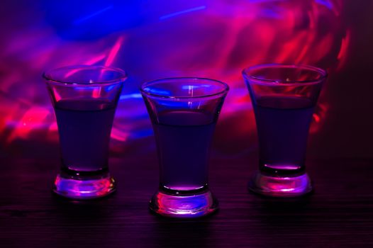 Three drinks at the party. Three shots with cocktails at the bar. Liquor, vodka, fresh. Shining on a colored background. Night club, after the party.