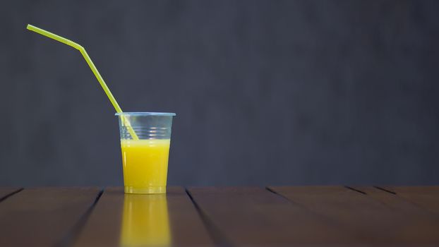 Orange juice in a plastic Cup with a tube on a brown background. Copy space. Picnic, vegan, healthy food, drink. Reuse and recycling of food grade plastic