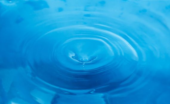 A splash of blue water. A drop of water on a blue background. Splashing, water surface, the funnel.