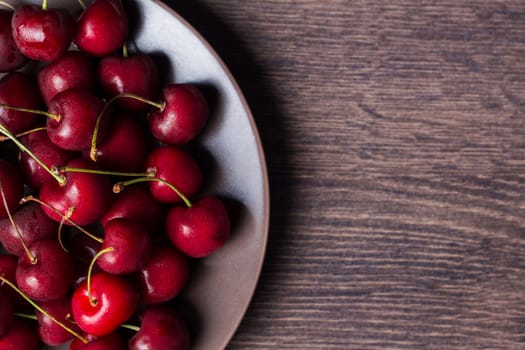 Cherries on a brown plate. Food with copyspace on a wooden table. Berries, snacks, healthy food. Vegan, vegetarian, diabetic, fruit.
