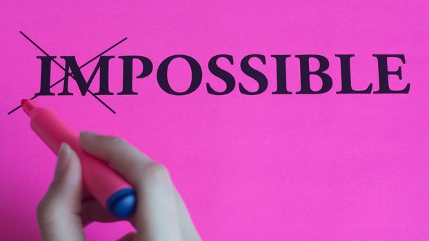 Motivational inscription impossible is possible on a pink background. Coaching, trainings, affirmations. Woman hand writes the word. hand writes marker on pink paper, text, message, art, study,