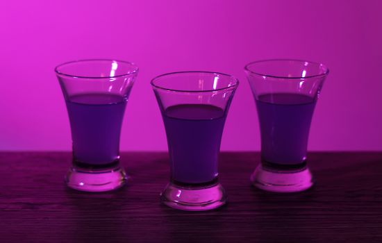 Three drinks at the party. Three shots with cocktails at the bar. Liquor, vodka, fresh. Shining on a colored background. Night club, after party.