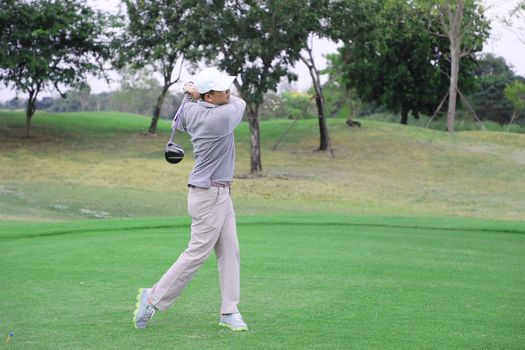 Asian golfer teeing off golf ball from tee box with his golf club