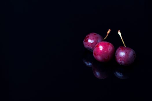 Three cherries on a black mirror background. Reflection, close-up, copy space. Berries, snacks, healthy food. Vegan, vegetarian, diabetic, fruit.