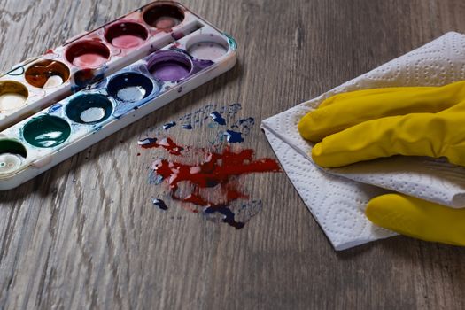 A hand in a yellow protective glove wipes the stain from the paints with a paper towel, a napkin.The woman does the cleaning. Clean, house, housekeeper, cleanup and housework.