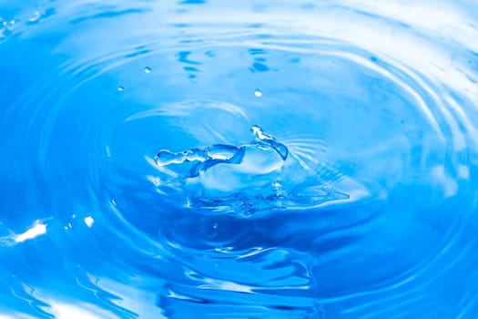 Water drops on blue surface. Water ripple background. Splashes from a drop of water. Raindrops on a blue background. The texture of the water. Aqua, turquoise, macro