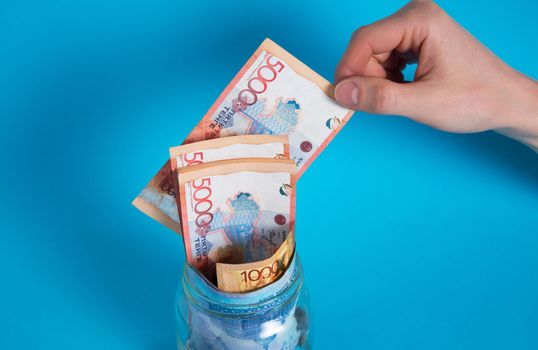 Get tenge out of a glass jar. Put money in a glass jar. Kazakhstan, KZ, KZT. Banknote, paper currency, coins, Bank. Salary, credit, savings, pay and spend. Business and Economics.
