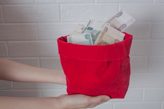 Hands hold a red bag with a lot of Rubles in it. Russian. National currency, banknote. Much money. Business, Economics, and investments. Wealth, accumulation, income.
