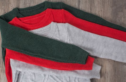 Clothing, fashion, style. Multicolored sweaters are placed on a wooden table. The clothes are neatly folded. Hygge, cozy, cashmere, soft. Home routine, order, storage of things.
