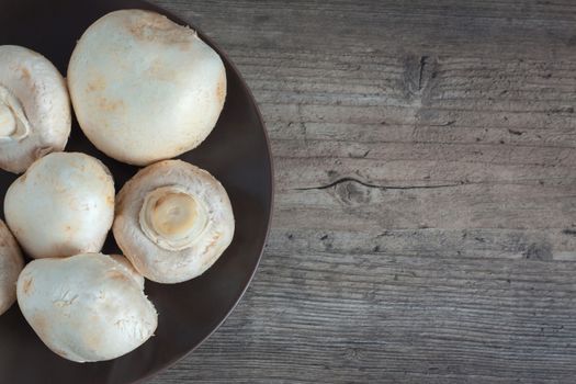 Mushrooms close-up on a wooden table. Champignon on a brown plate. Dietary, vegan, vegetarian, diabetic. Ingredients, recipes. Food, cooking, food. Copy space, clear space, top view.
