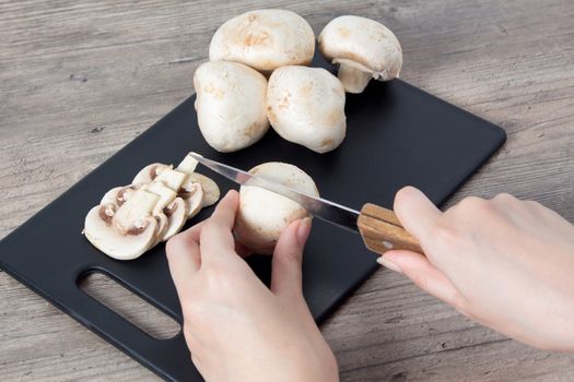 Food. To cook the champignon. Hand cuts mushrooms with a knife on a black cutting Board. Vegan, vegetarian. Top view, close-up