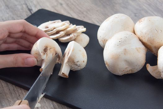 Pieces of champignon mushrooms. The girl cuts mushrooms into halves with a knife. Cooking by a female chef. Top view on a black cutting Board. Food, vegan, vegetarian, dietary.