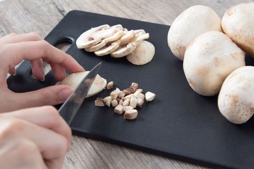 Cutting mushrooms with a knife on a black cutting board. Food. To cook the champignon. Vegan, vegetarian. Close-up.