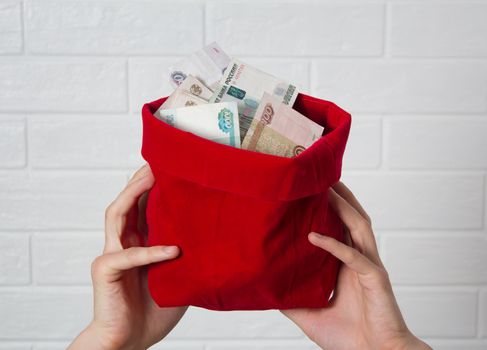 Hands holding a red bag with rubles. Much money. Banknote, the national currency of Russia. Bank, economy, business. Savings, salary, winnings, jackpot.