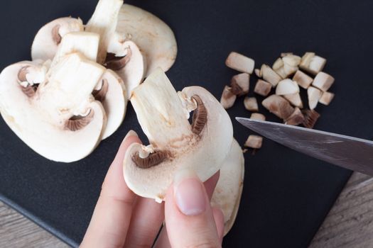 Pieces of champignon mushrooms. The girl cuts the mushrooms into even pieces with a knife. Cooking by a female chef. Top view on a black cutting Board. Food, vegan, vegetarian, dietary.