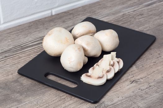 Champignon mushrooms on a black cutting Board. Cook food. Vegetarian, vegan, dietary, proper nutrition, healthy lifestyle. Edible mushrooms cut into even slices.