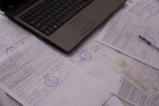 Office Desk with papers, receipts and documents. Work with documents at the plant or enterprise. Laptop or computer on the office Desk with documents. Job.