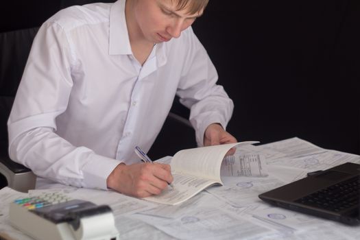 White man working in an office with documents. The Manager makes the report and fills in the Declaration. Businessman at work in his workplace. Young guy at the table with a laptop and cash register.