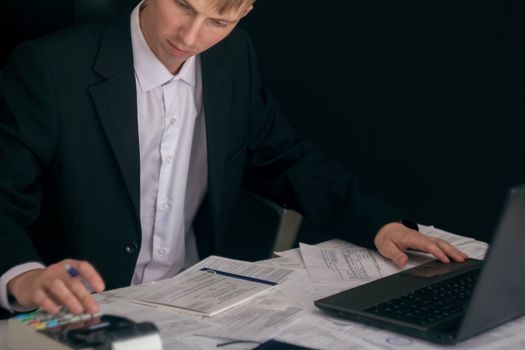 White man working in an office with documents. The Manager makes the report and fills in the Declaration. Businessman at work in his workplace. Young guy at the table with a laptop and cash register.