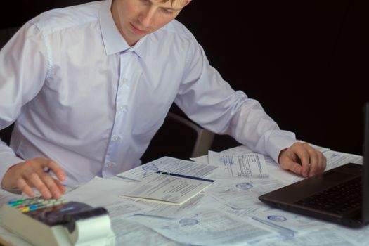 The Manager makes the report and fills in the Declaration. Businessman at work in his workplace. Young guy at the table with a laptop and cash register.businessman working with documents in office.