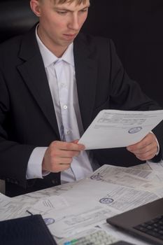 Businessman signing a contract. The Manager makes the report and fills in the Declaration. Businessman at work in his workplace. Young guy at the table with a laptop, cash register documents.