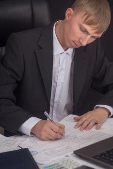 Businessman signing a contract. The Manager makes the report and fills in the Declaration. Businessman at work in his workplace. Young guy at the table with a laptop, cash register documents.