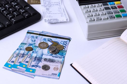 Tenge on a white table with a cash register. Cashier's workplace in Kazakhstan. Salaries in Kazakhstan