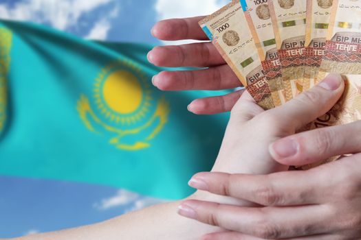 Paper banknotes tenge KZT people hold in their hands on the background of the flag of Kazakhstan. Tenge is the national currency of Kazakhstan.