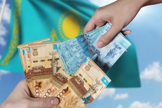 Paper banknotes tenge KZT people hold in their hands on the background of the flag of Kazakhstan. Tenge is the national currency of Kazakhstan.