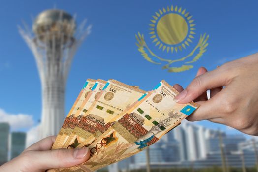 Tenge paper banknotes people hold tenge in their hands on the background of Baiterek in Astana and the flag of Kazakhstan. Tenge is the national currency of Kazakhstan.