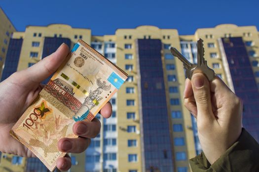 Buying a new apartment in Kazakhstan for tenge. New Buildings In Kazakhstan. Real estate services and Bank loans. He had the keys and the money tenge in his hand against the backdrop of the new house