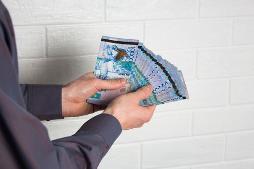 Guy holding money Tenge from the outside against a brick wall. Paper banknotes tenge KZT. Tenge is the national currency of Kazakhstan. bank of Kazakhstan