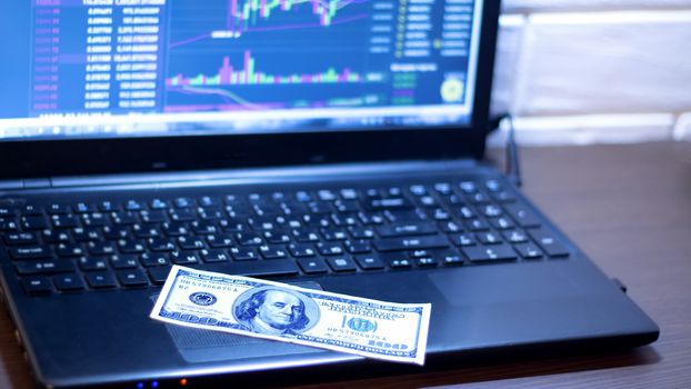 a hundred-dollar bill is placed on a laptop with a price chart for Forex, the market, stocks, bonds, or securities. Working place of a trader