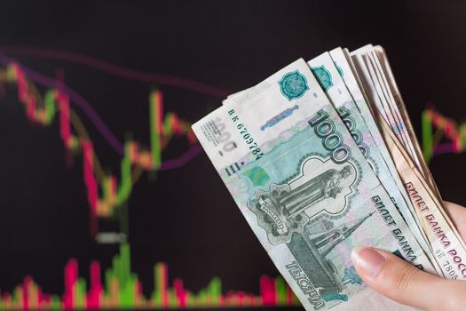 Hands holding Russian rubles in front of a computer monitor with the currency market and Forex trading chart. Trading stocks, bonds, and securities on the stock exchange. Trader in Russia with ruble.