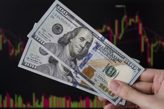 Hands holding dollars in front of a laptop monitor with a price chart.Forex and trading.A trader trades stocks,bonds and securities or currencies on the Forex market or stock exchange for us dollars.