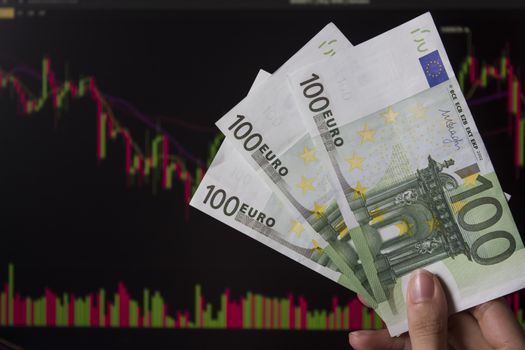 Hands holding euro, EUR in front of a laptop monitor with a price chart.Forex and trading.A trader trades stocks,bonds and securities or currencies on the Forex market or stock exchange for euro