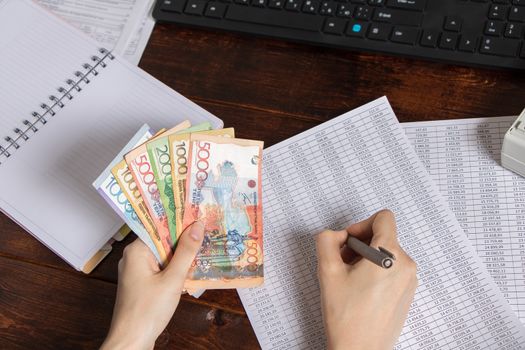 Hands hold Tenge KZT banknotes are next to the computer, Notepad and documents. Paper banknotes tenge KZT. Bank of Kazakhstan