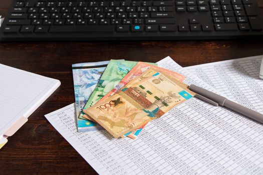 Tenge of KZT are on the table next to the computer, Notepad and documents. Paper banknotes tenge KZT. Bank of Kazakhstan